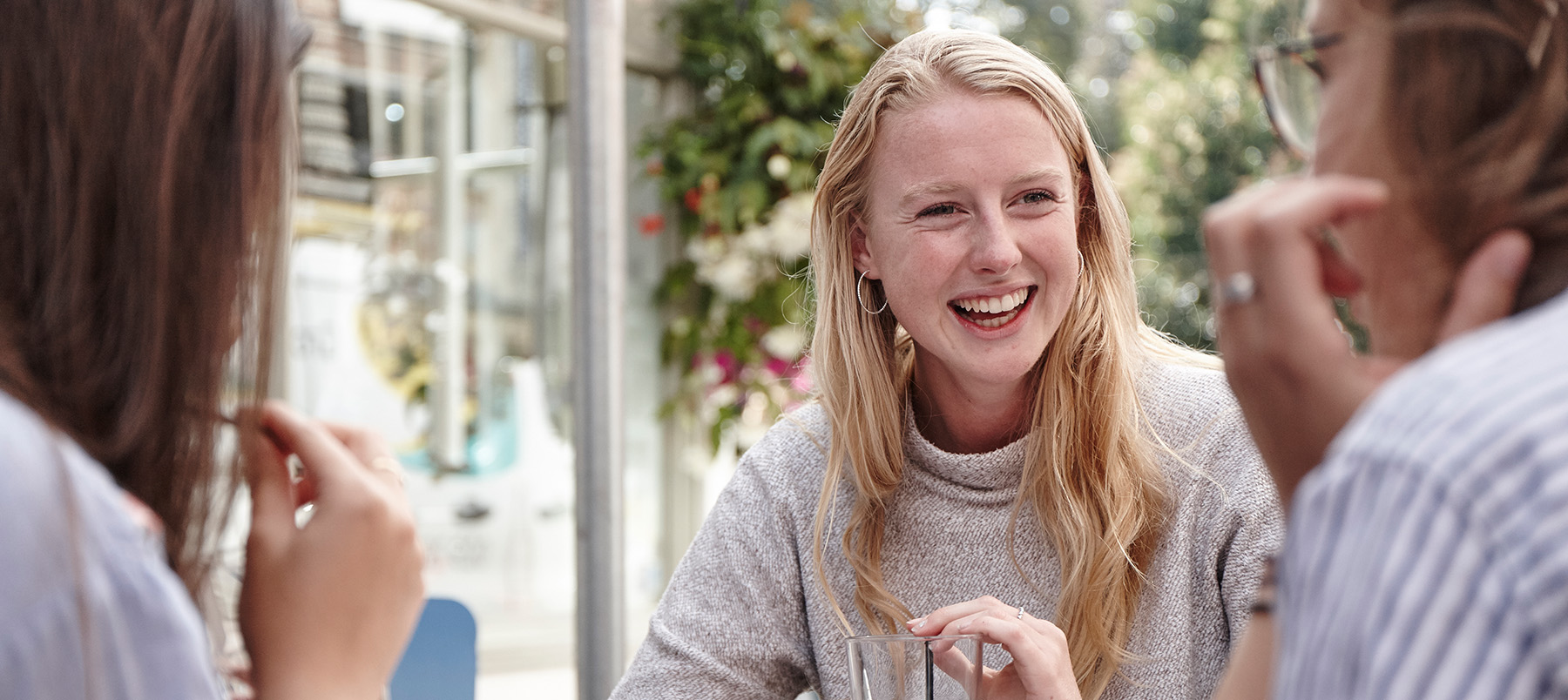 Female student sat at a coffee table smiling and having a conversation with a student to her right