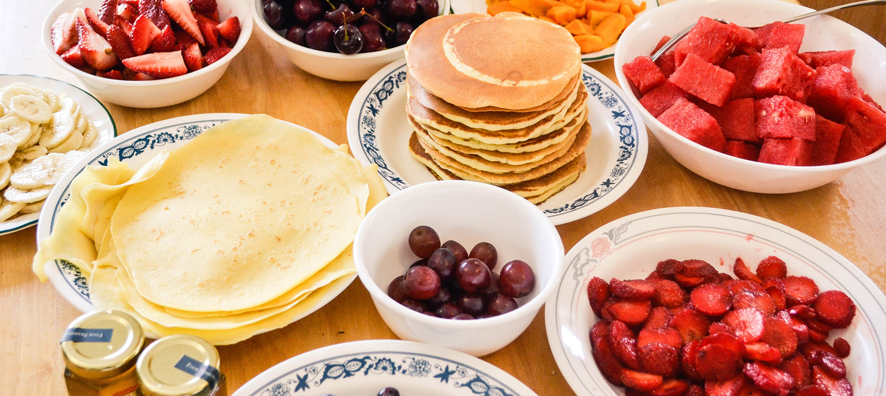 Pancakes and fruit in plates and bowls on a table