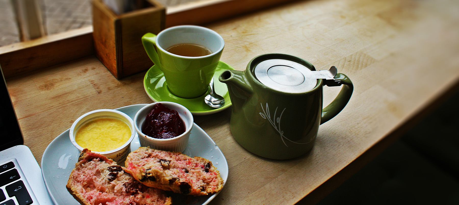 Food and a mug of tea on a table next to a laptop