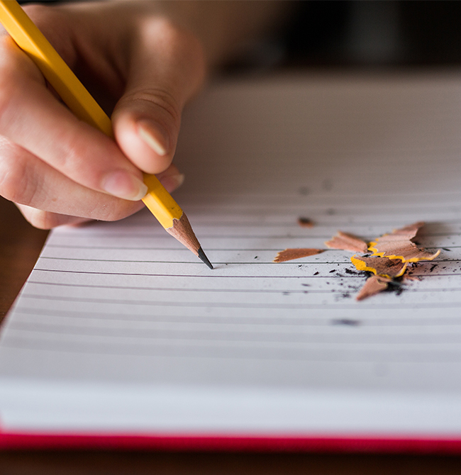 Person writing in a notepad with a pencil, pencil sharpenings on the paper