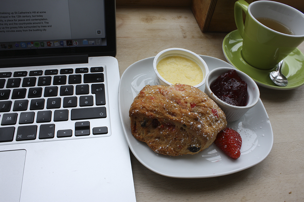 Fruit muffin and cup of tea on a table next to a laptop