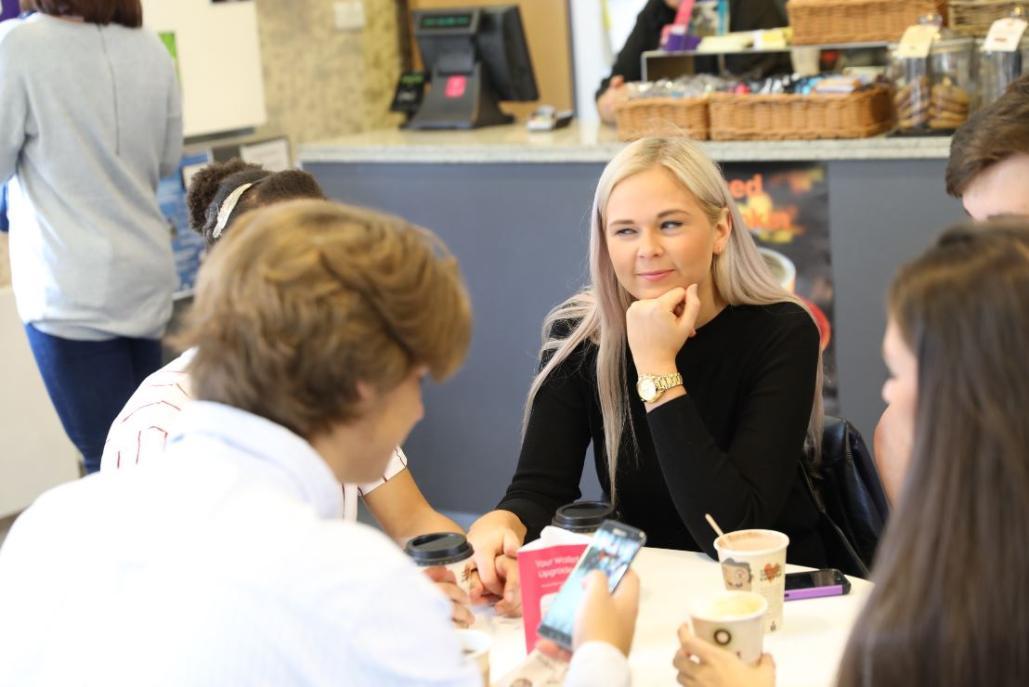 A group of students sat in a cafe around a table with coffee mugs on