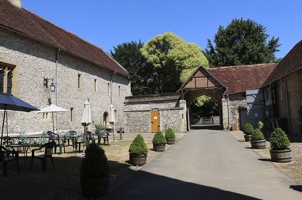 Inside of a courtyard for an old stoney building, cafe tables setup with umbrellas