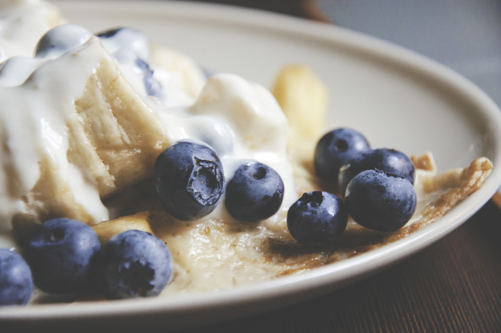 Close up of pancakes on a plate with banana and blueberries on top