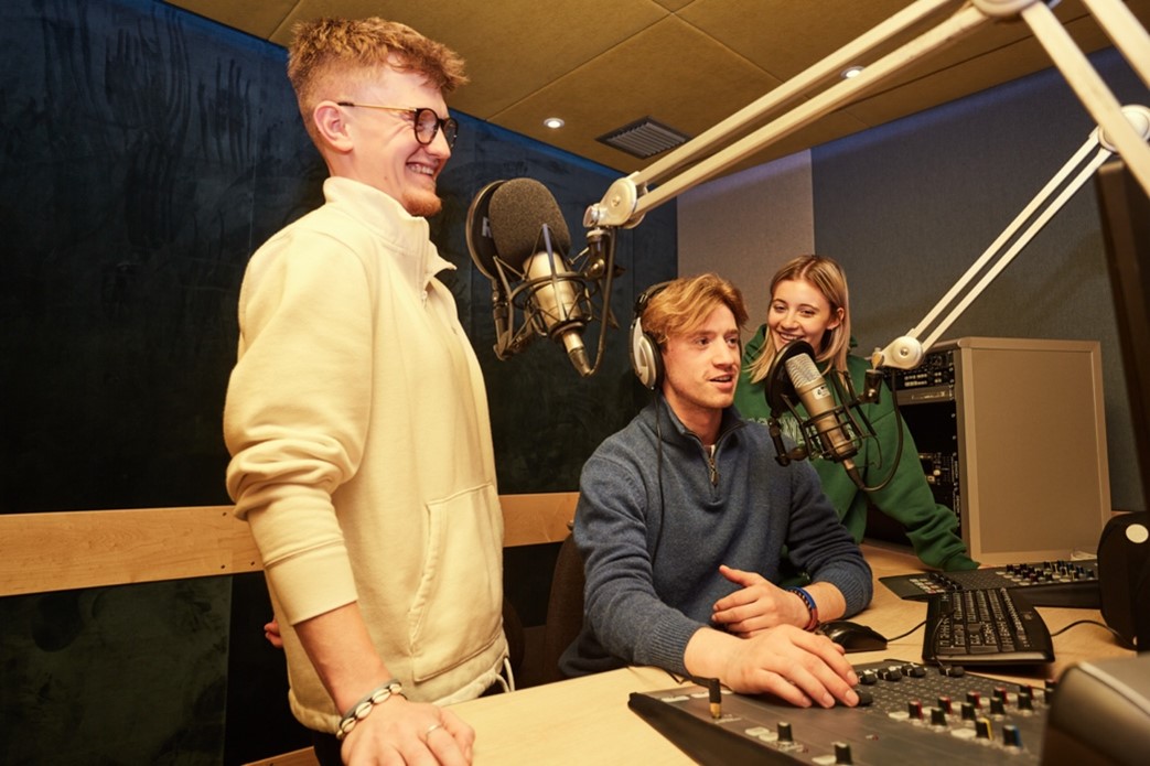 A group of students in a radio booth speaking into a microphone