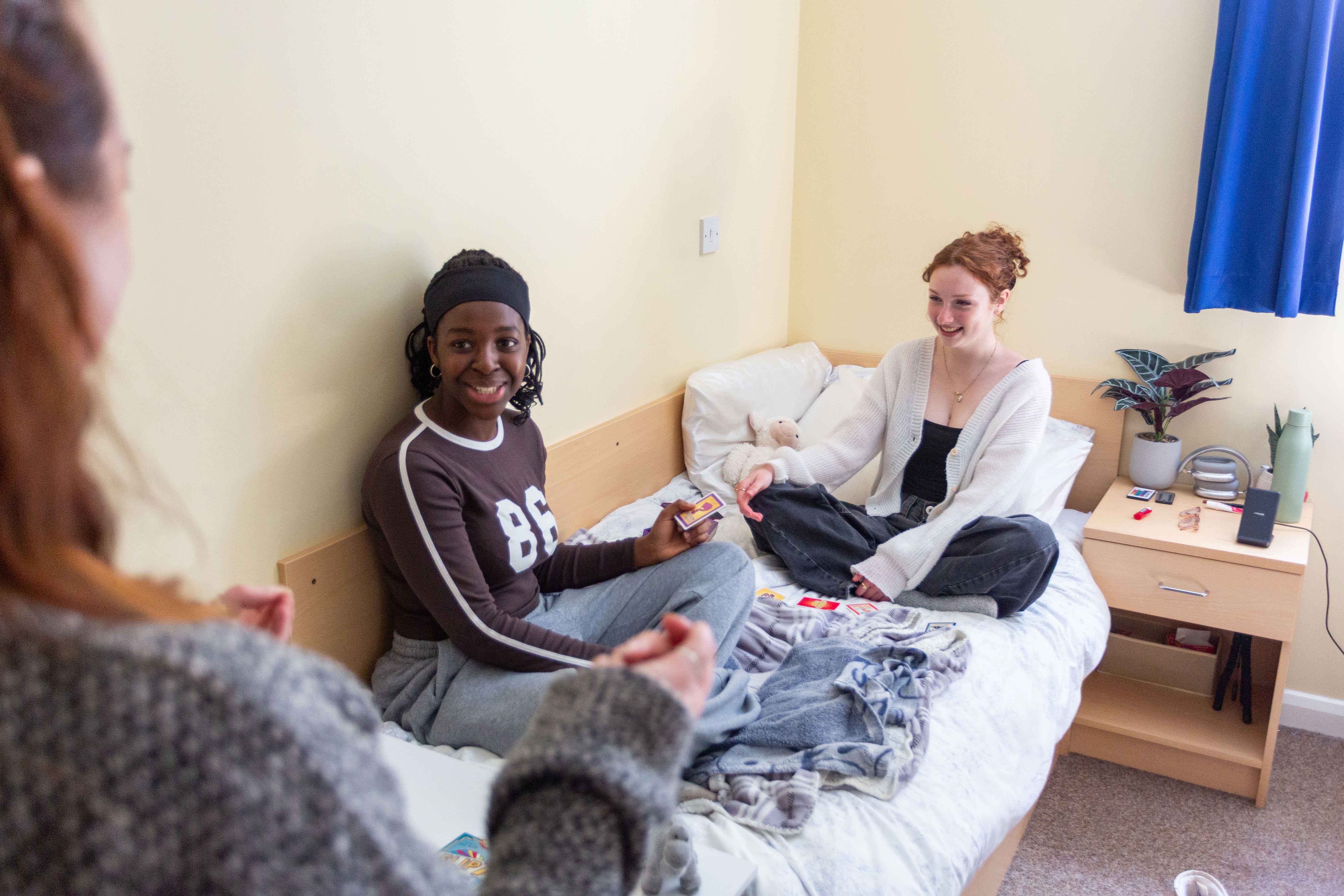 Two students sitting on a bed within university accommodation