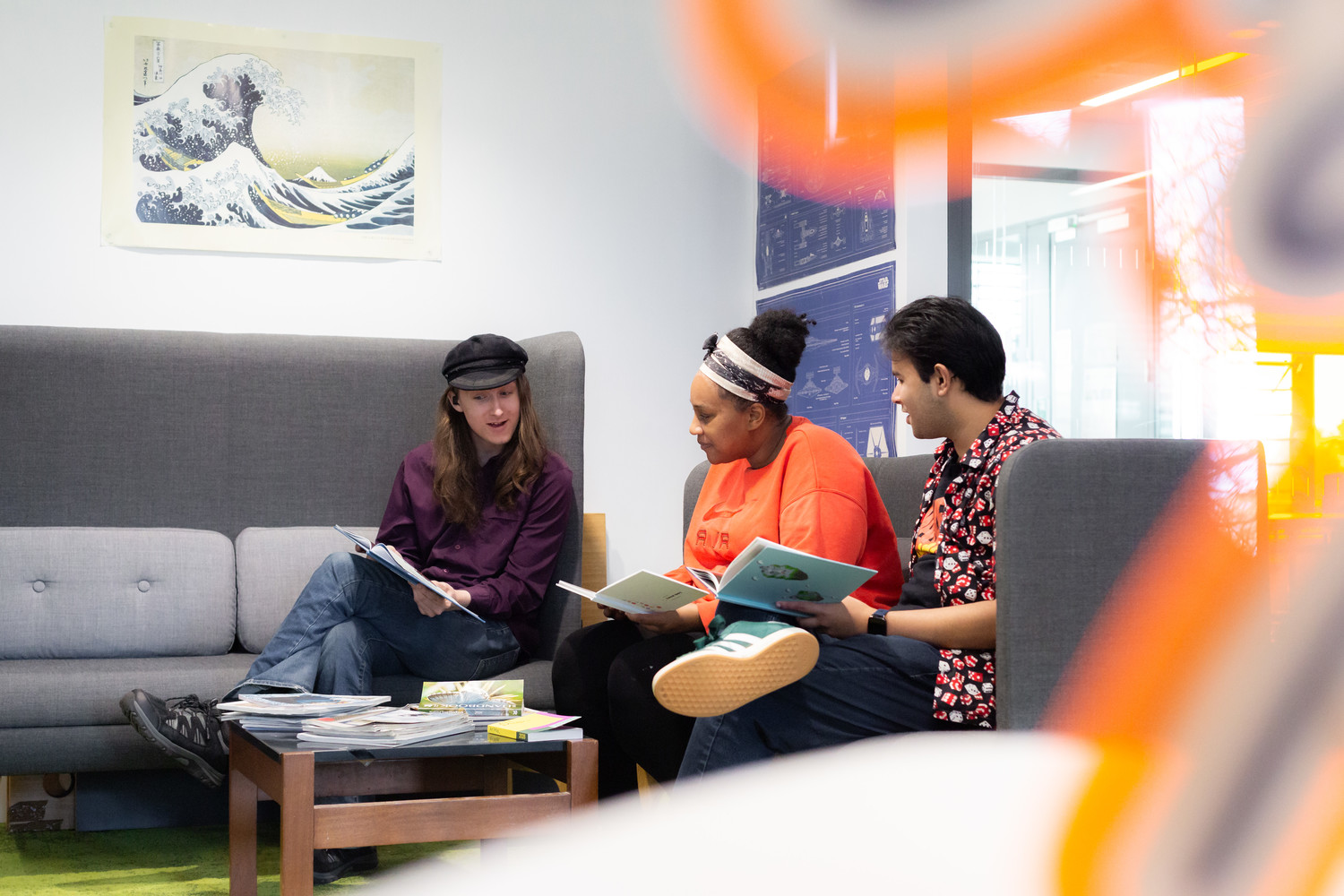 Three students look at journals together sat around a coffee table