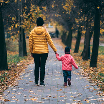 Mother and young child holding hands walking along a path in autumn landscape