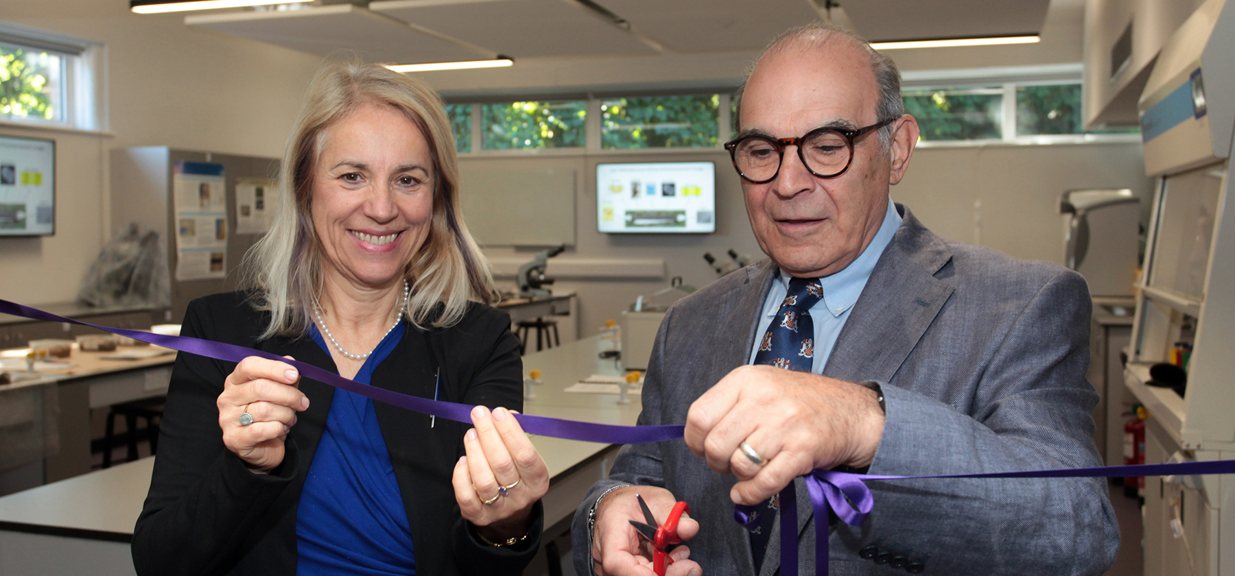 David Suchet cutting a purple ribbon in the forensics lab