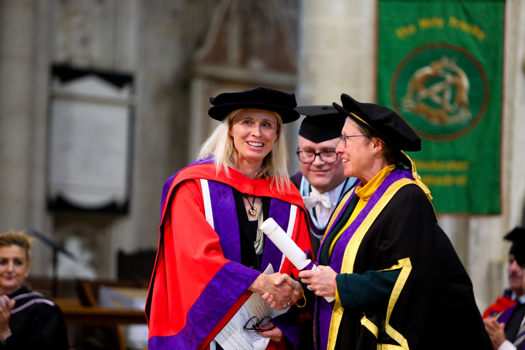 Honorary doctor in red robers receives her scroll from elderly academic in black robes