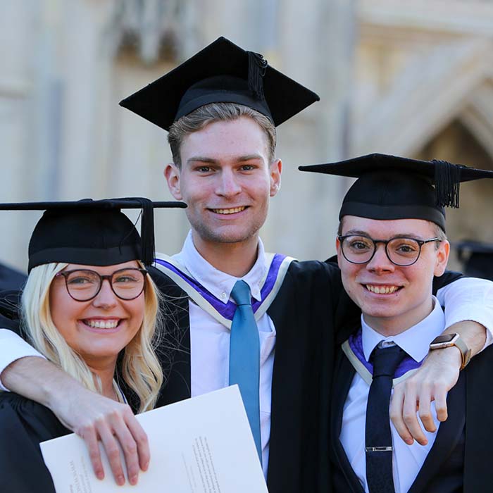 Three students in graduation robes standing with their arms around each other