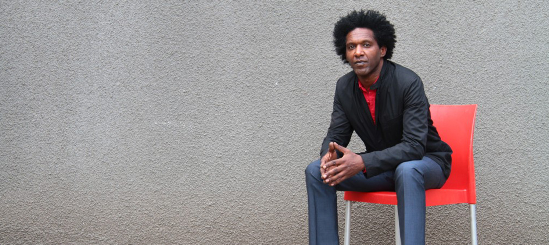 Lemn Sissay sitting on red chair