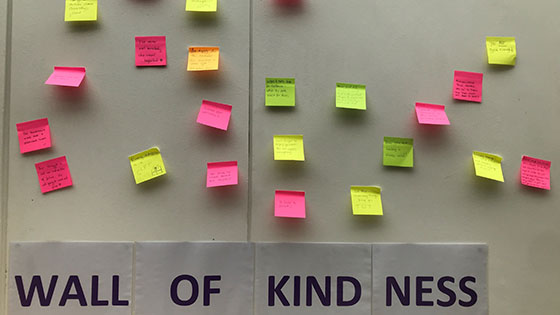Wall of kindness with messages written on pink, yellow and green post it notes