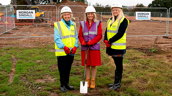 Joy Carter with spade and two councillors in hard hats and hi vis jackets on construction site