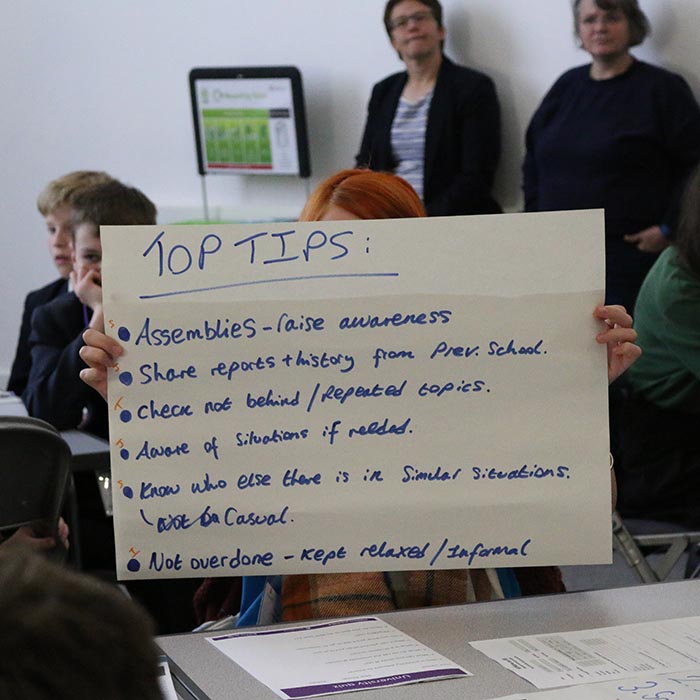 Pupil holds up large piece of paper with top 10 tips written in black ink