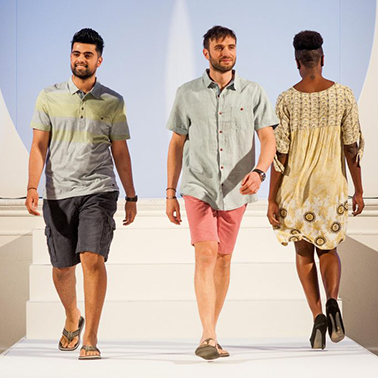 Two men and a woman walk along a catwalk wearing colourful summer clothes