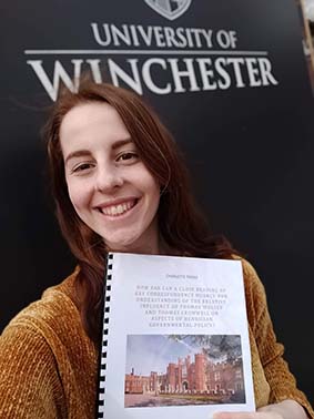 Young woman holding her dissertation in front of University of Winchester sign