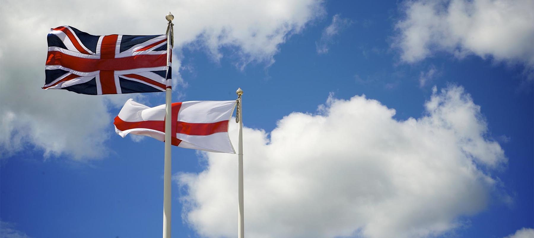 English and British flags fly side by side against blue skies
