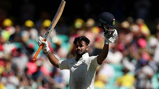 Cricketer Rishabh Pant holding his bat and helmet aloft on the field of play