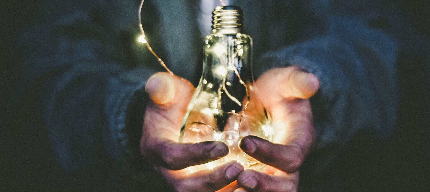 Close up of hands holding lightbulb with fairy lights inside