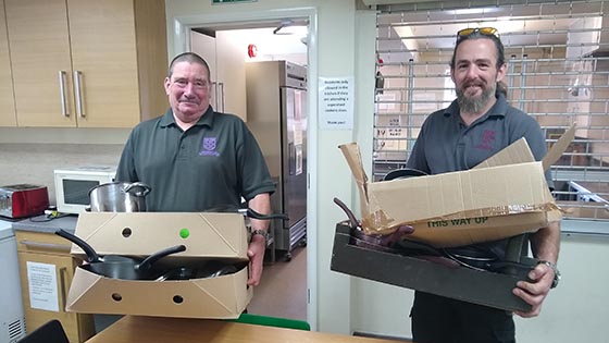 Two University porters holding boxes of donated kitchen equipment at The Winchester beacon