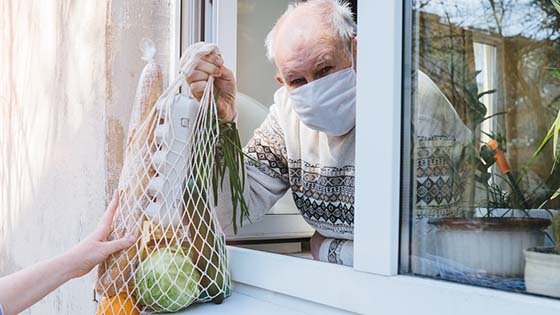 Old man with mask on receives groceries in drawstring bag through open window