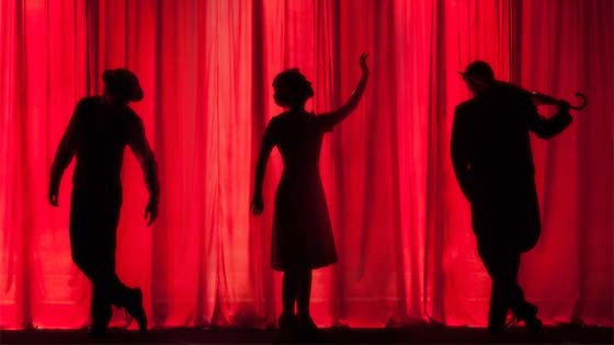 Three silhouettes lit behind red curtain