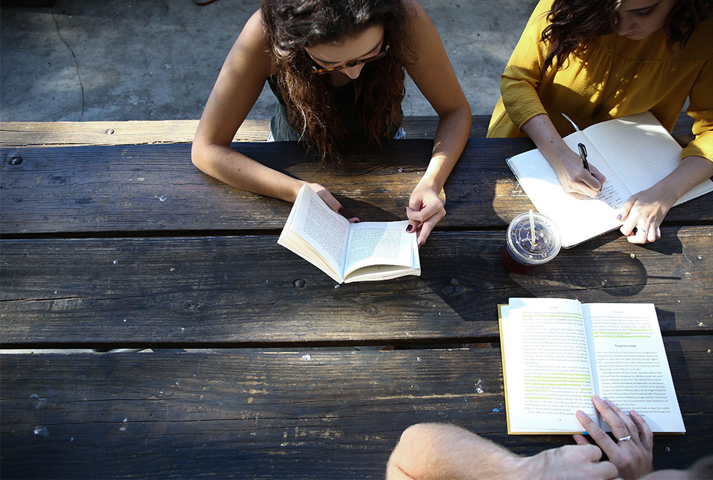 Three students sat on a bench reading books