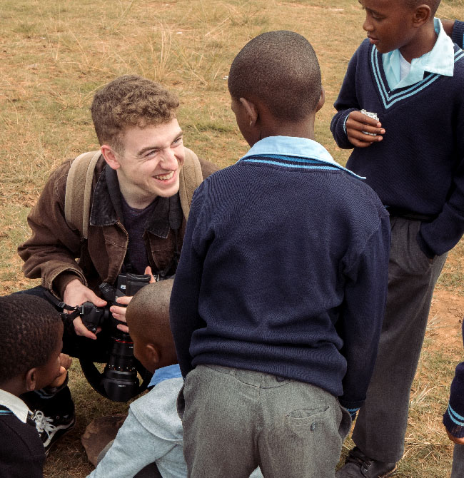 Film production student holding a camera and talking to South African children